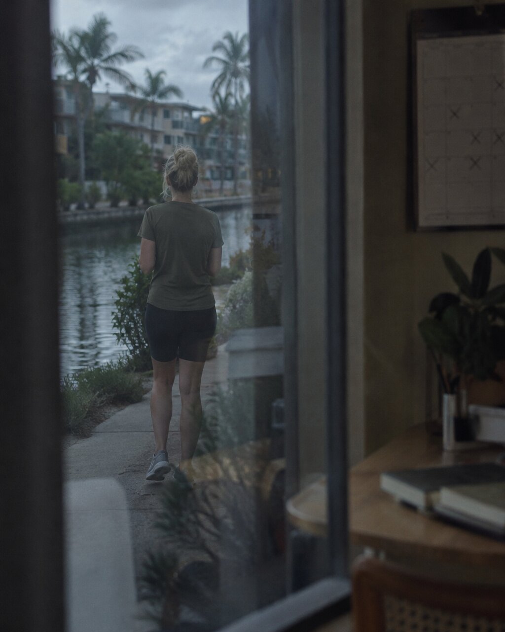 Woman seen from behind walking along a canal path, viewed through a window
