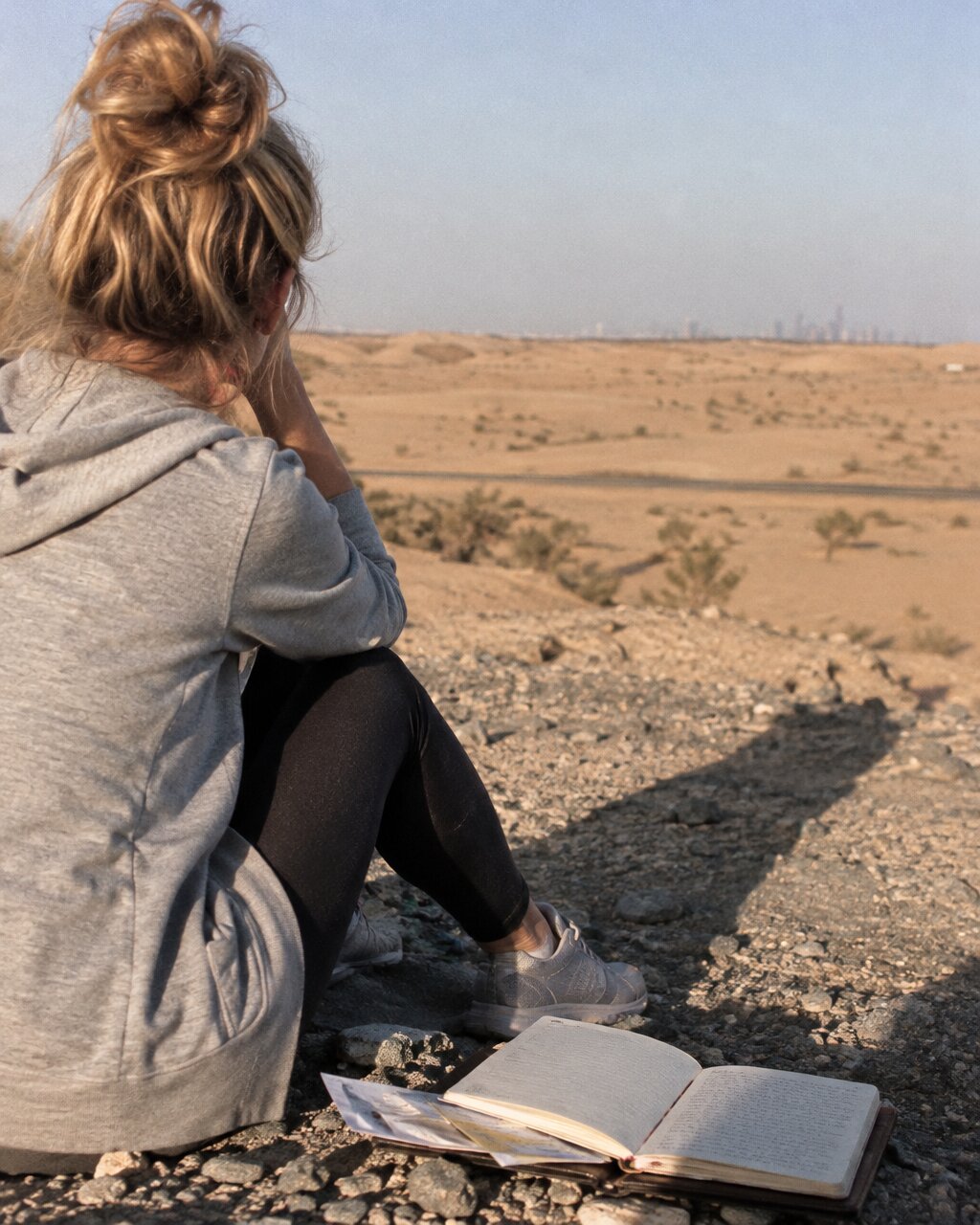 Woman seen from behind sitting beside an open book, looking across a desert landscape