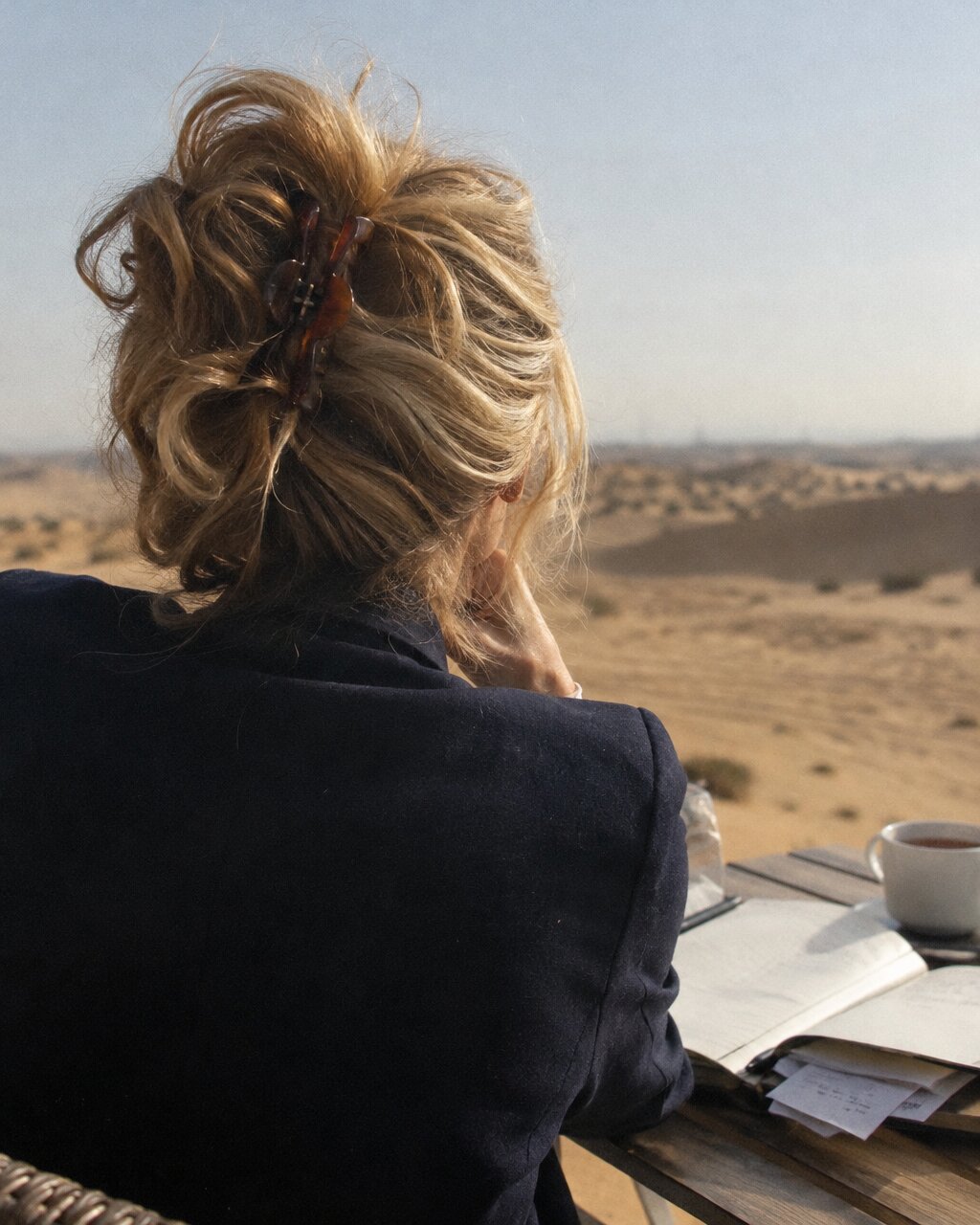 Woman seen from behind, sitting at a table with a notebook, overlooking a desert