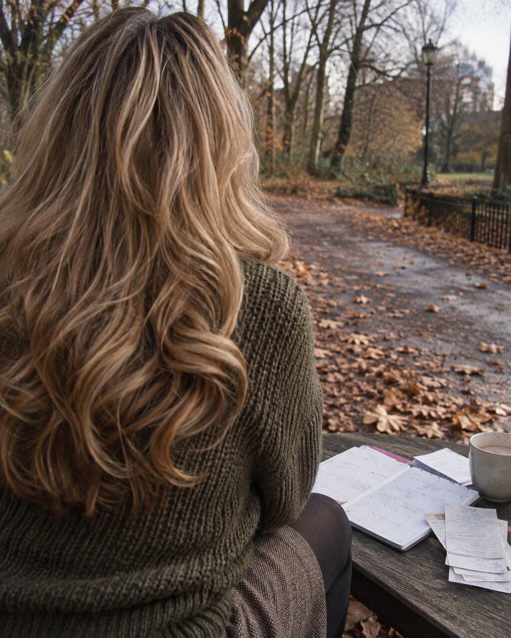 Woman seen from behind, sitting at a park table with a notebook in autumn